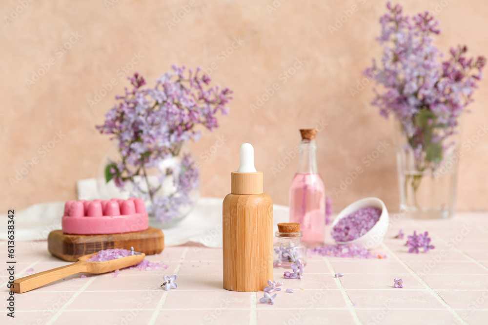 Bottles of cosmetic oil with beautiful lilac flowers and sea salt on pink tile table