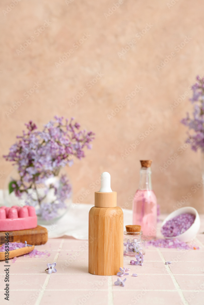 Bottles of cosmetic oil with beautiful lilac flowers and sea salt on pink tile table