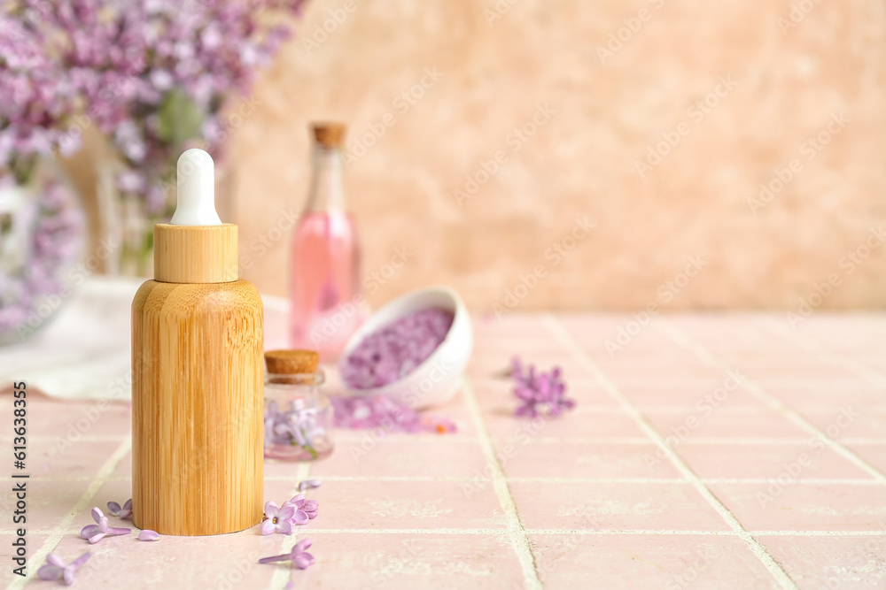 Bottles of cosmetic oil with beautiful lilac flowers and sea salt on pink tile table