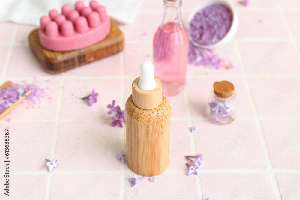 Bottles of cosmetic oil with beautiful lilac flowers and sea salt on pink tile table