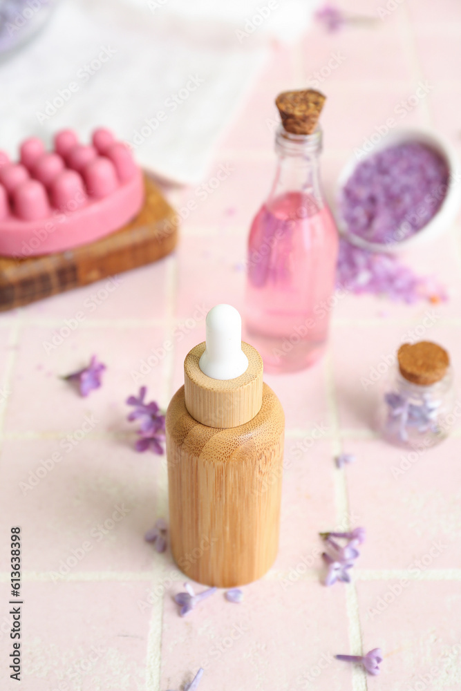 Bottles of cosmetic oil with beautiful lilac flowers and sea salt on pink tile table