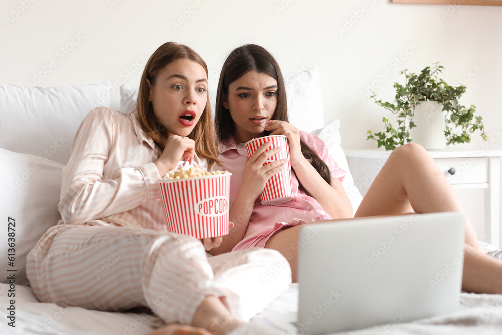 Scared female friends with popcorn watching movie in bedroom