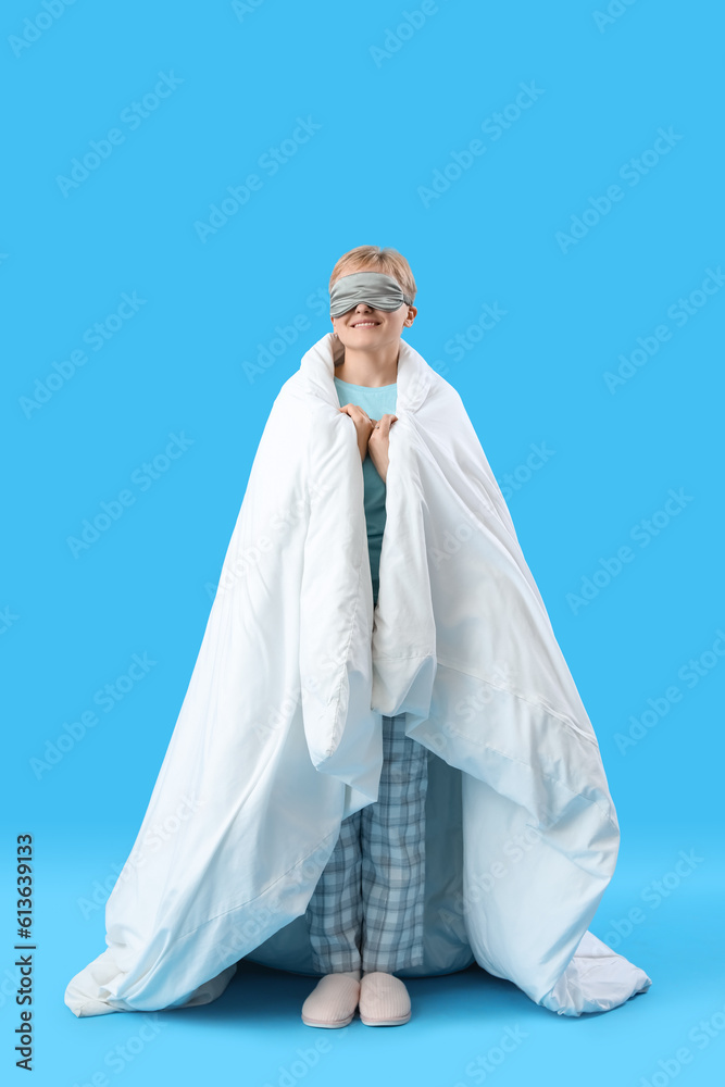 Young woman in sleeping mask with soft blanket on blue background