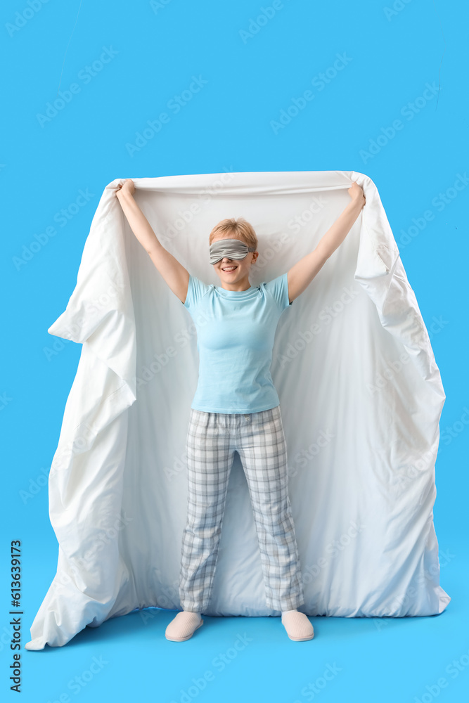 Young woman in sleeping mask with soft blanket on blue background