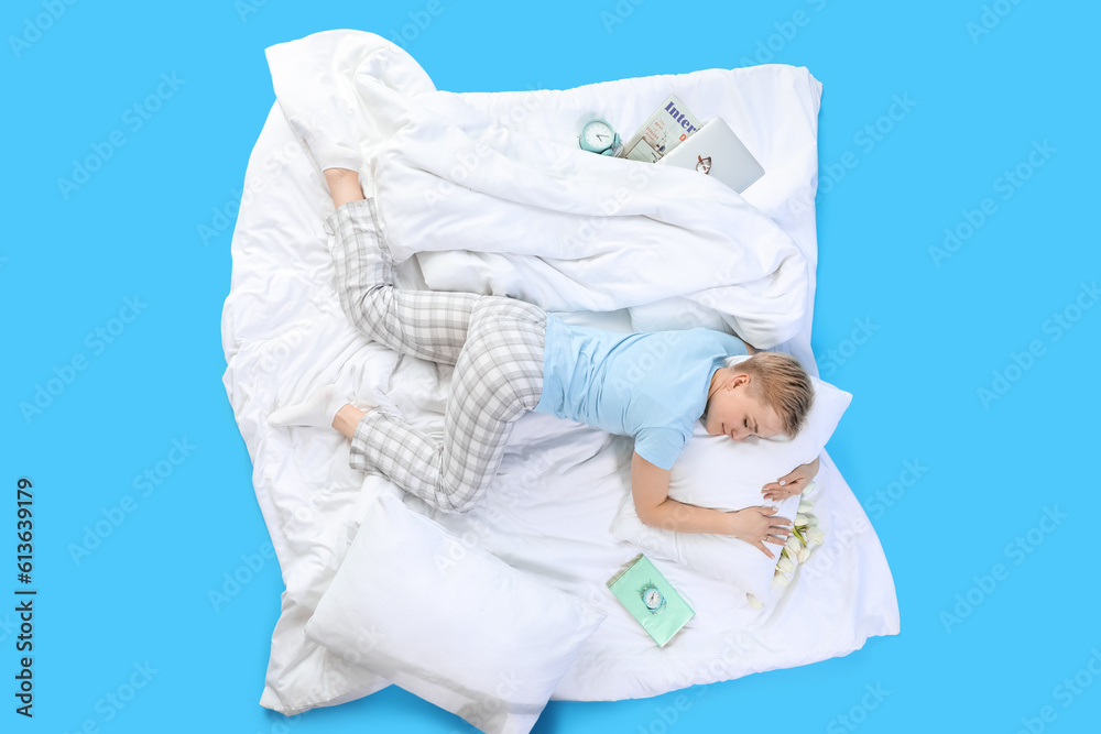 Young woman with pillow and soft blanket sleeping on blue background, top view