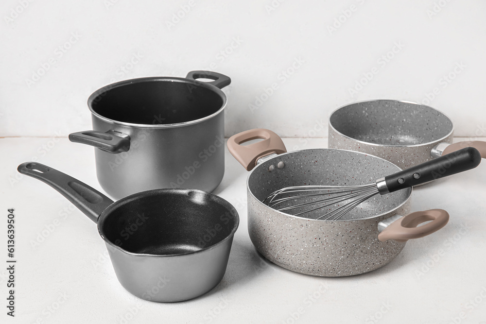 Set of cooking pots and whisk on light background