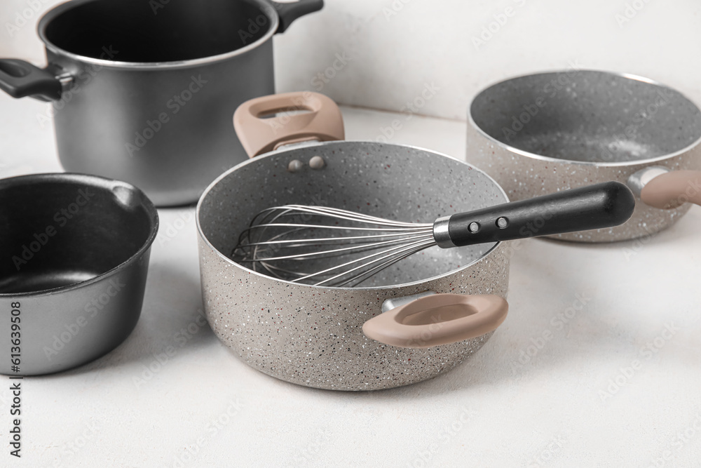 Set of cooking pots and whisk on light background, closeup