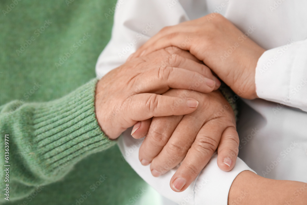 Senior woman with female doctor holding hands at home, closeup