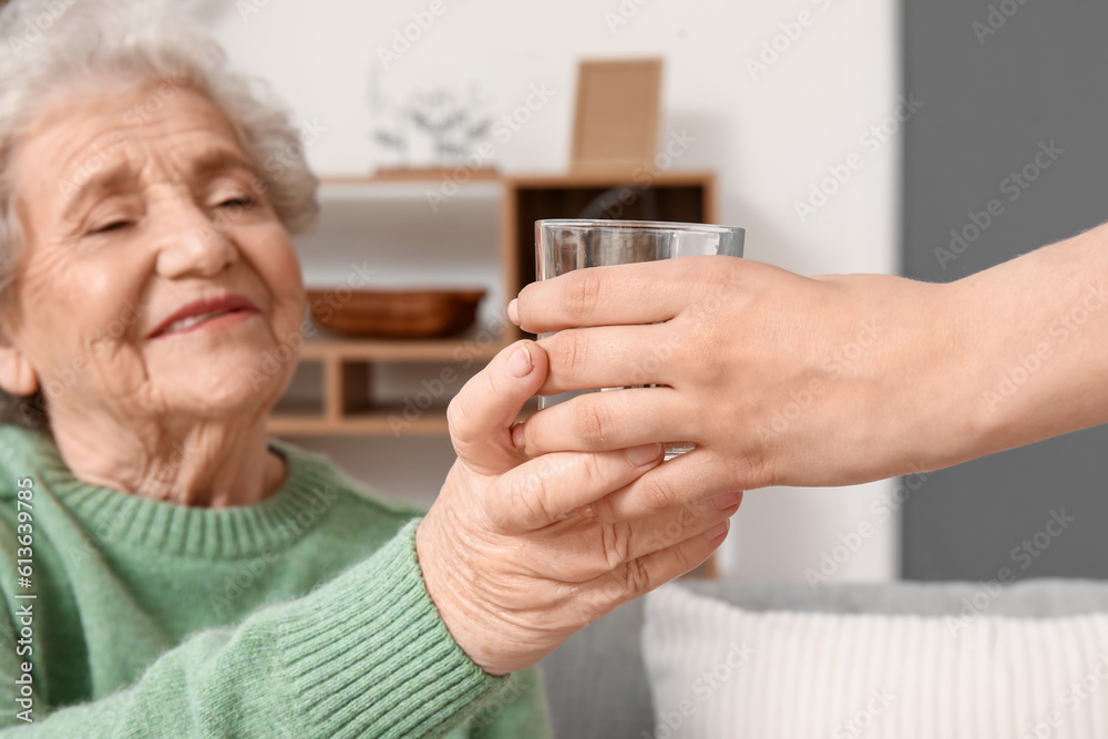 Young woman giving glass of water to her grandmother at home, closeup