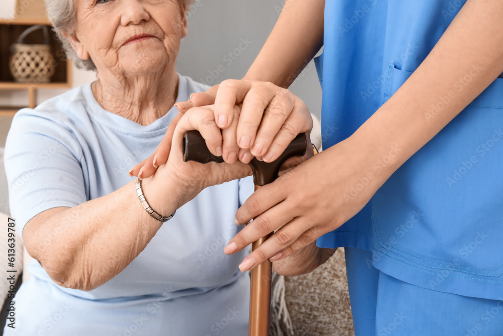 Senior woman with walking stick and female caregiver at home, closeup