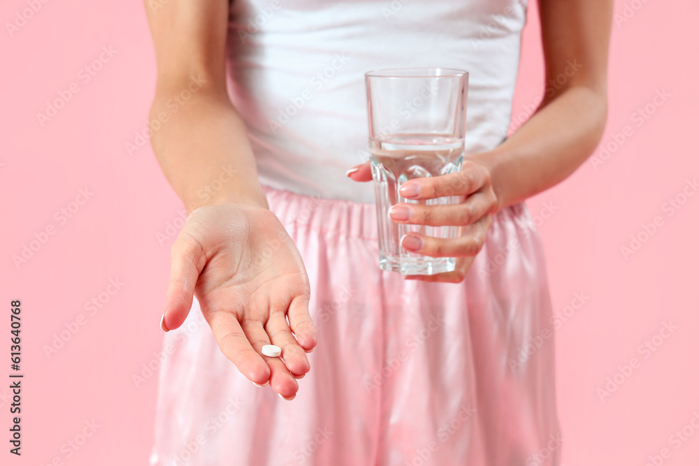 Young woman with pill and glass of water on pink background