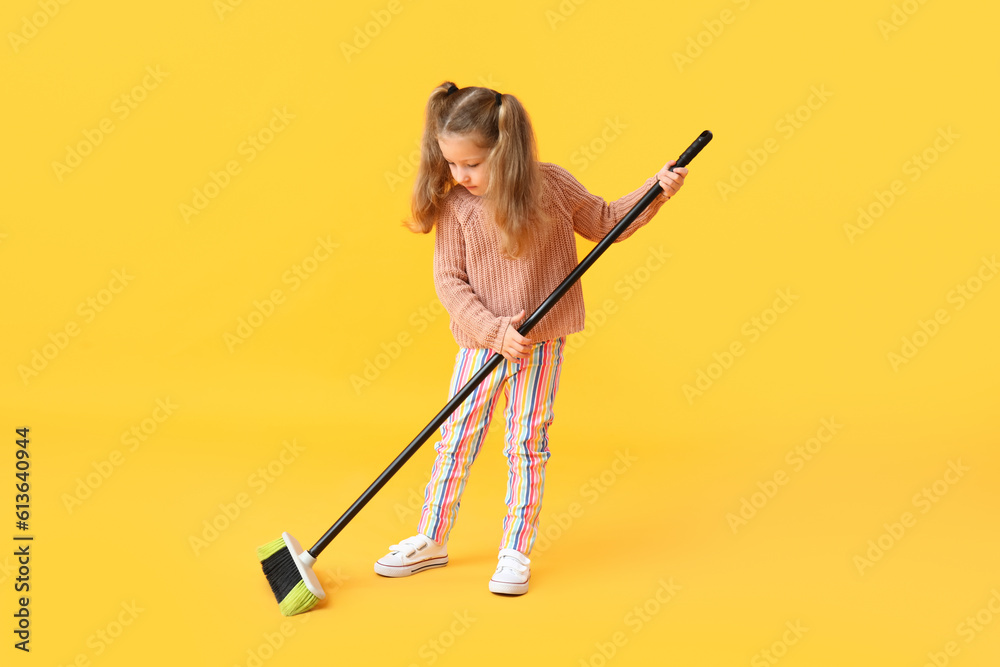 Cute little girl with broom on yellow background