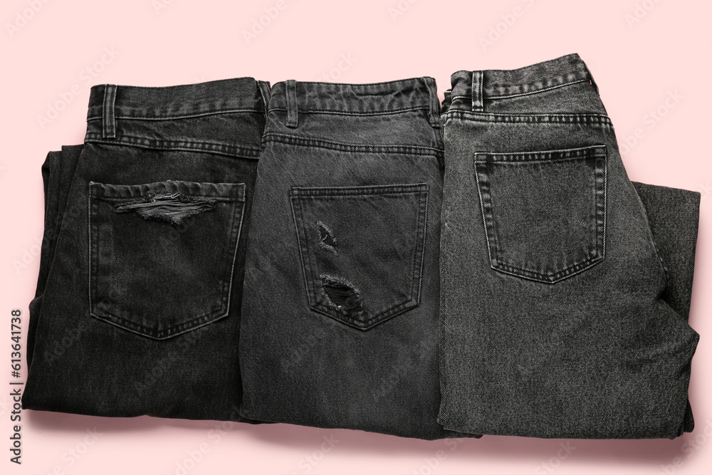 Different folded dark jeans on pink background