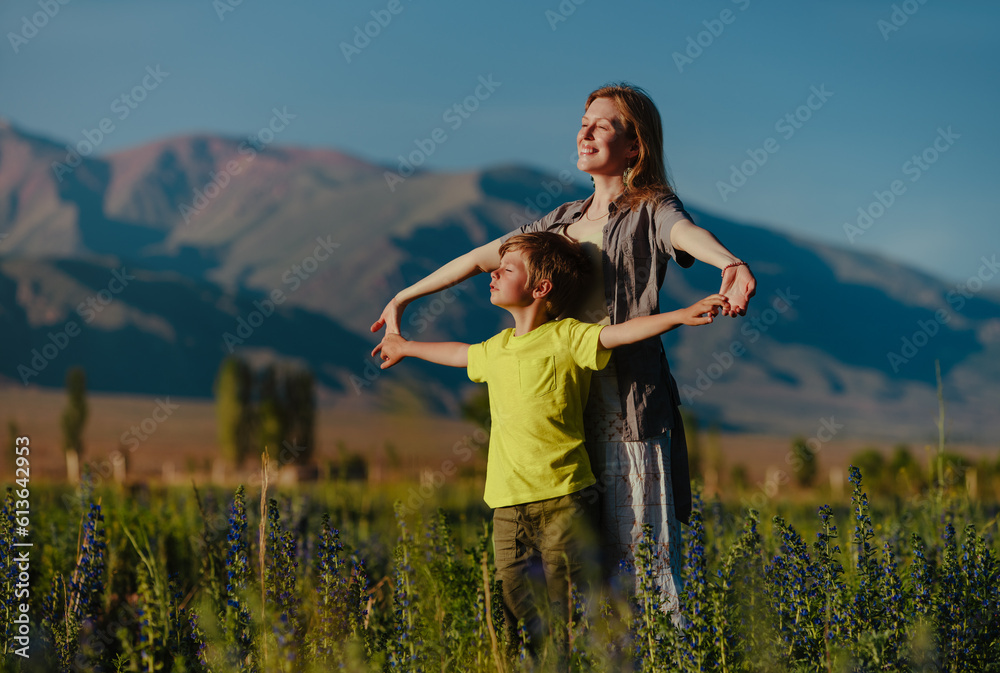 Happy young woman with her son posing in a blooming meadow on mountains background