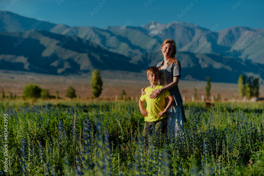 Happy young woman with her son posing in a blooming meadow on mountains background