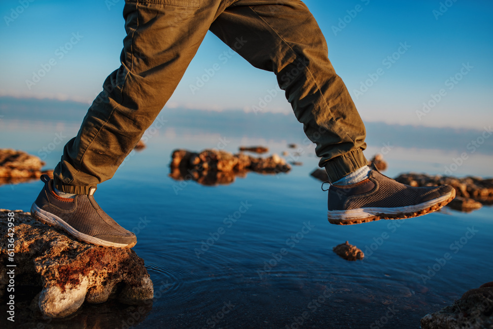 Boy walking on stones in the lake, close-up focus on boots