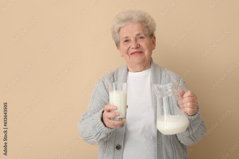 Senior woman with glass and jug of milk on beige background