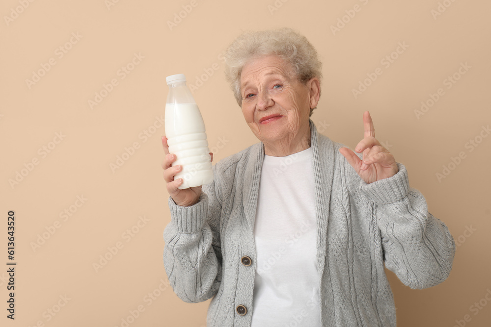 Senior woman with bottle of milk pointing at something on beige background