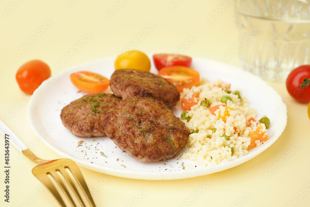 Cutlets with bulgur, boiled vegetables and tomatoes on light yellow table in kitchen