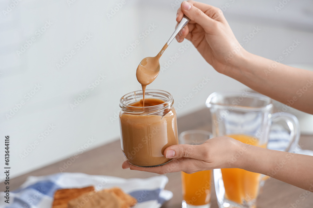 Young woman with spoon and jar of nut butter in kitchen, closeup