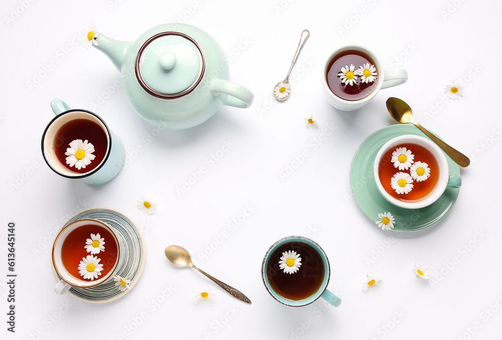 Frame made of teapot, cups with natural chamomile tea and flowers on white background