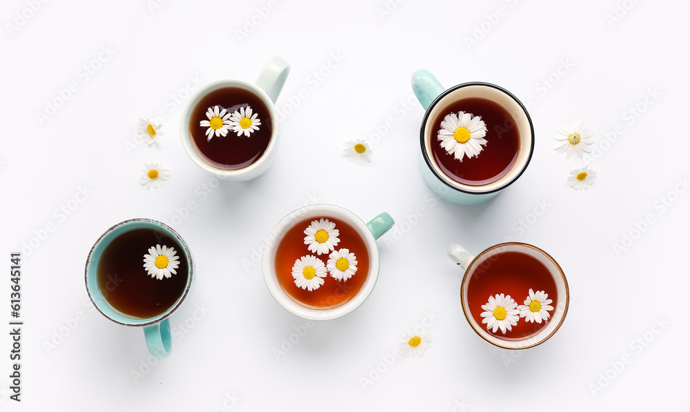 Cups of natural chamomile tea and flowers on white background