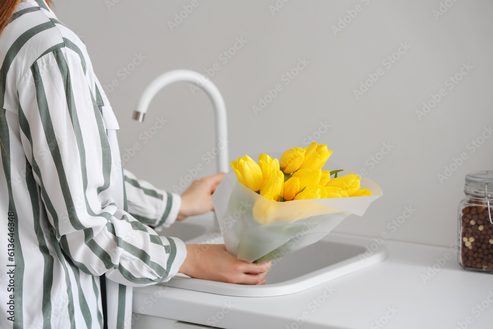 Woman taking bouquet of yellow tulip flowers from kitchen sink