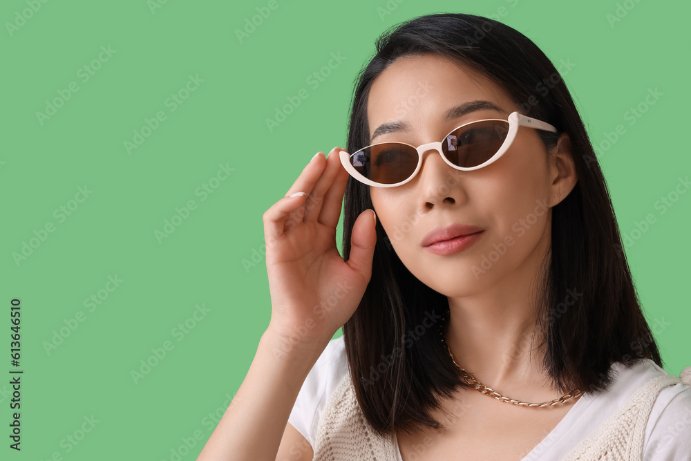 Beautiful Asian woman in stylish sunglasses on green background, closeup