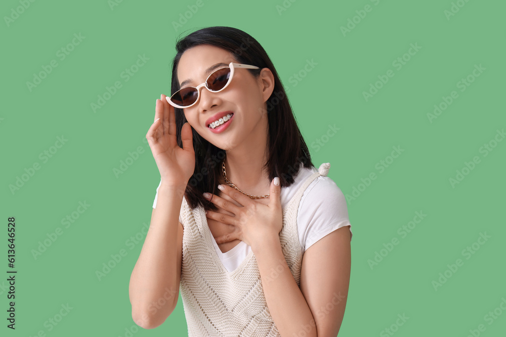 Beautiful Asian woman in stylish sunglasses on green background