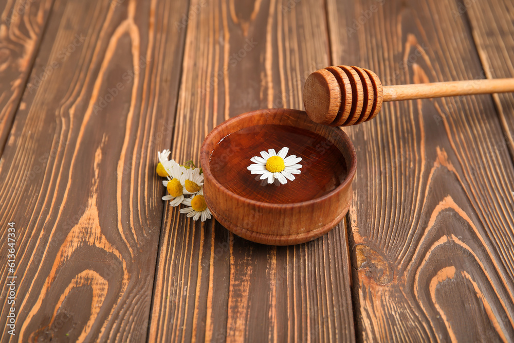 Bowl of water, chamomile flowers and honey dipper on wooden background