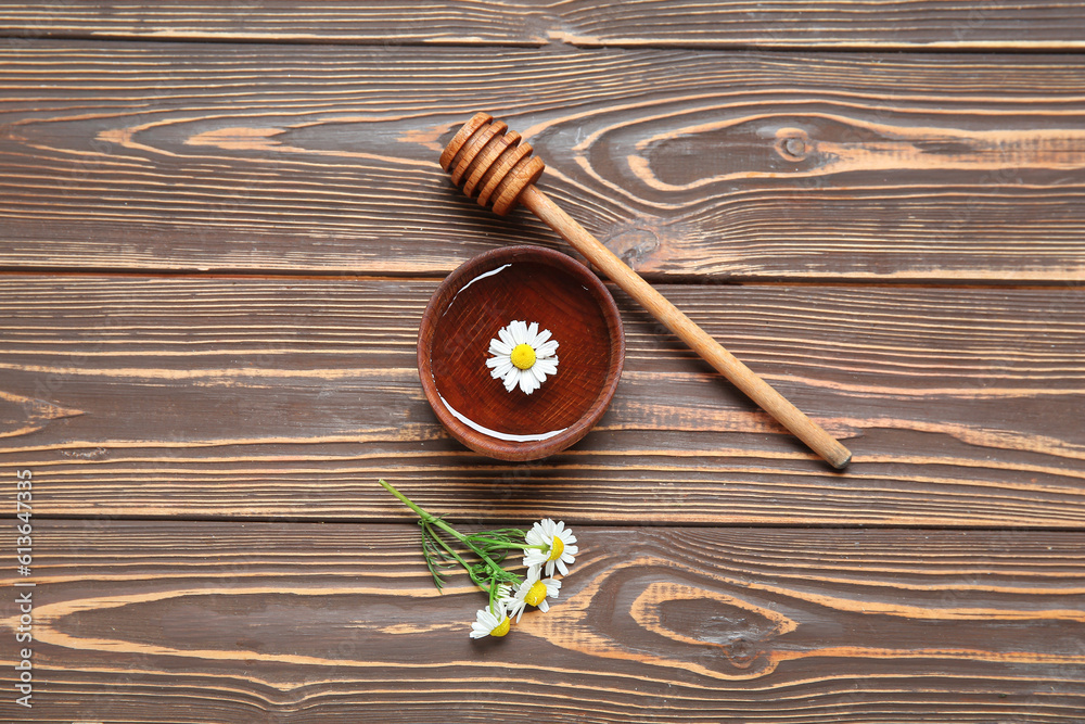 Bowl of water, chamomile flowers and honey dipper on wooden background