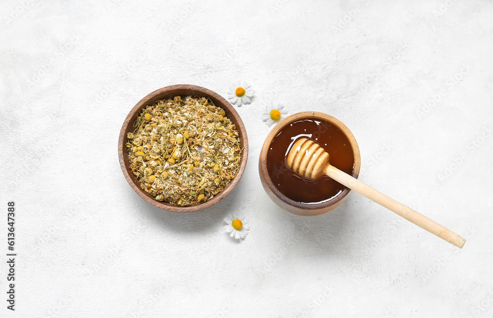 Bowls of honey and dried chamomile flowers on light background