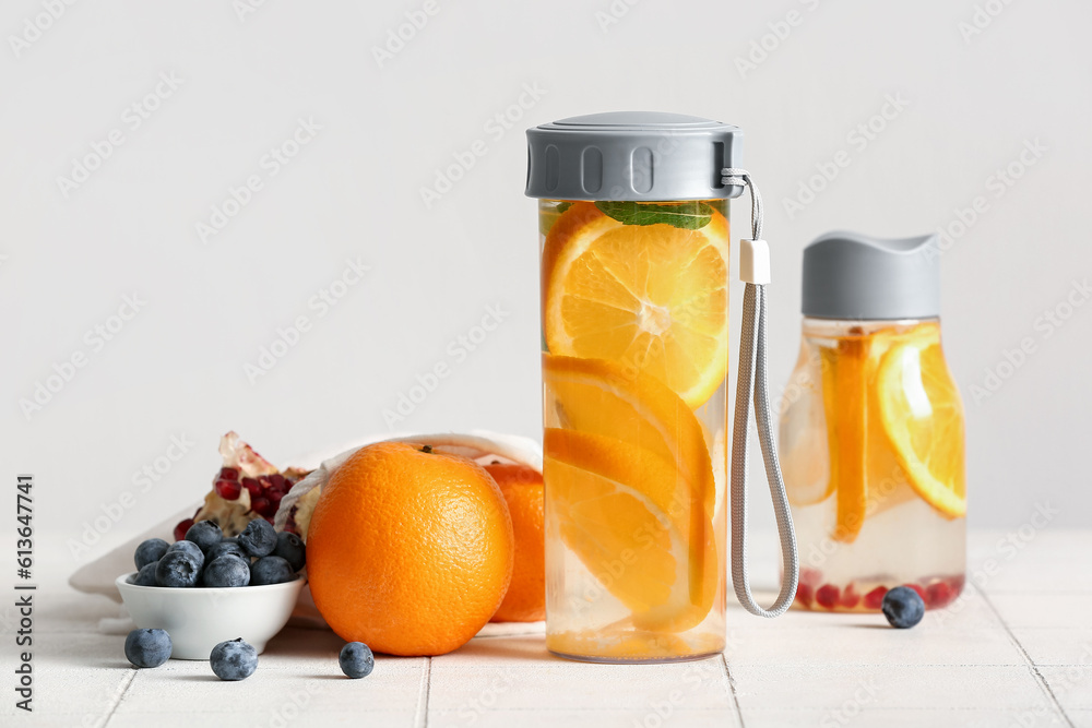 Sports bottles of infused water with orange slices on white tile table