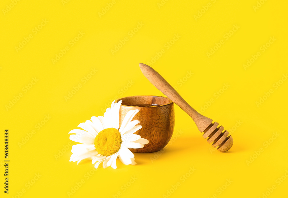 Bowl of honey and beautiful chamomile flower on yellow background