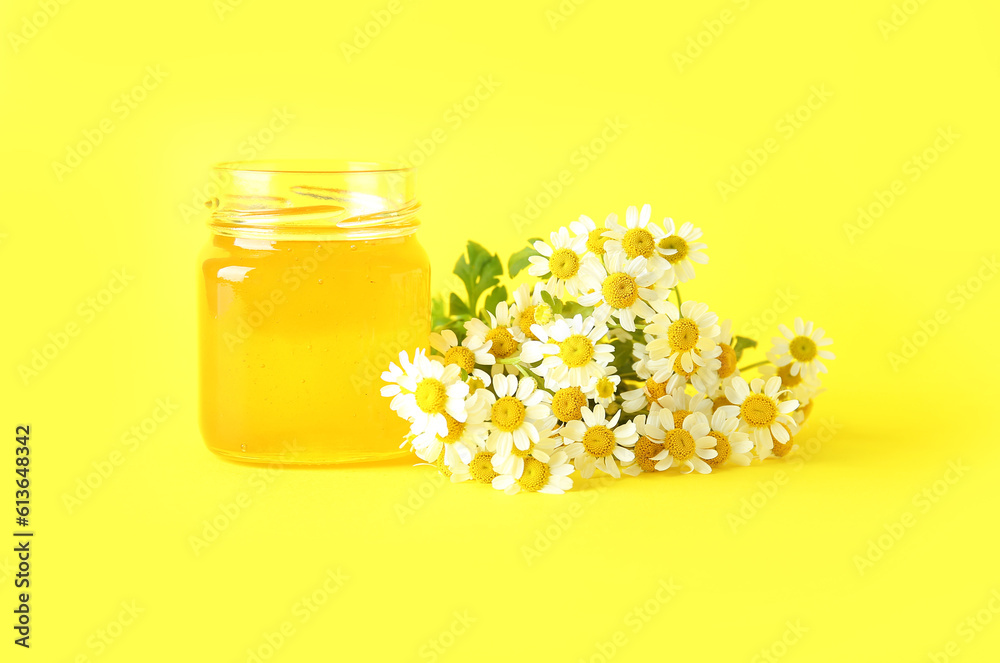 Jar of honey and beautiful chamomile flowers on yellow background