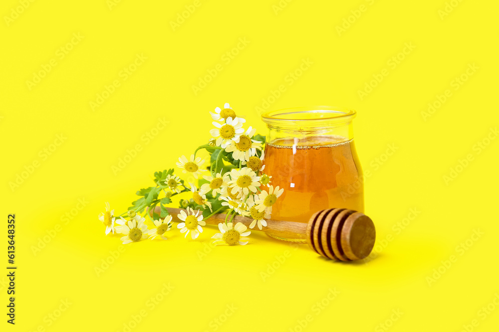 Jar of honey, dipper and fresh chamomile flowers on yellow background