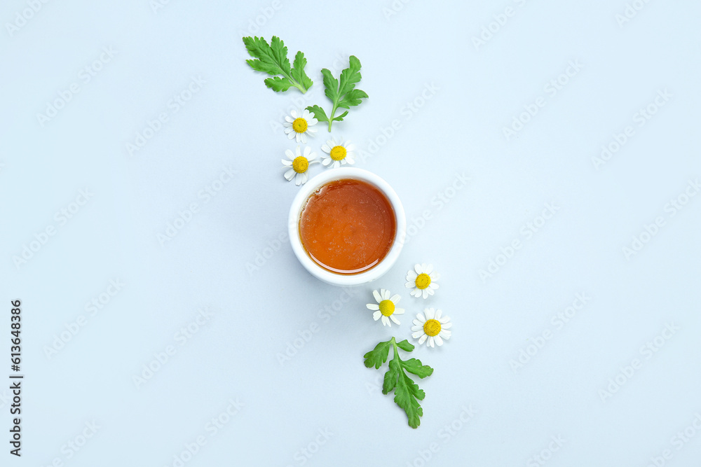 Composition with bowl of honey, chamomile flowers and leaves on light background