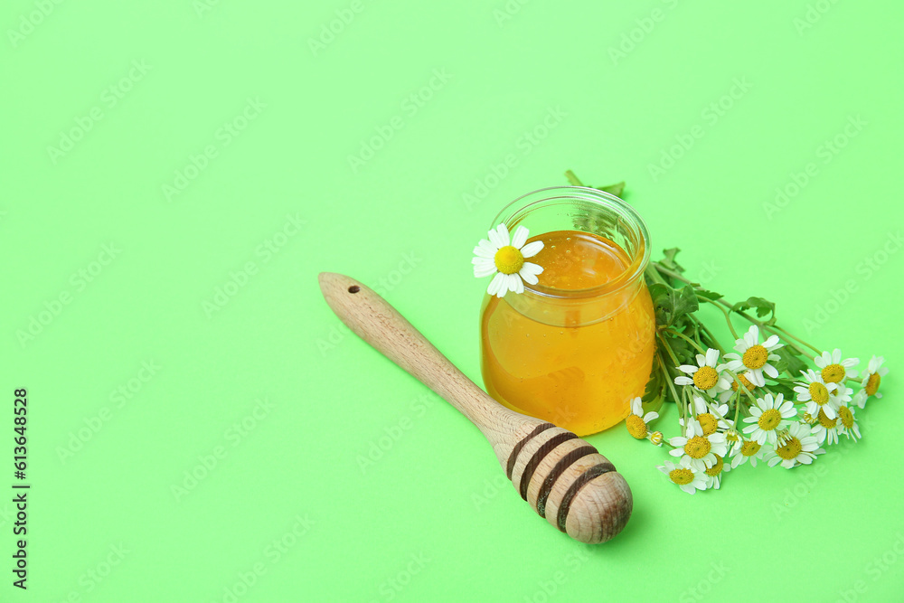 Jar of honey, dipper and fresh chamomile flowers on green background