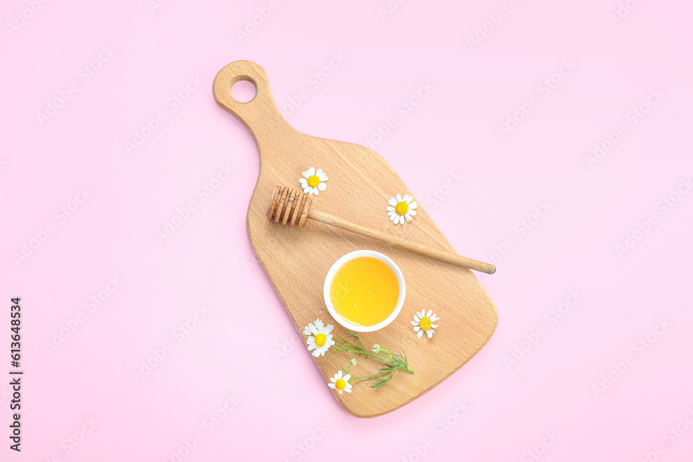 Wooden board with bowl of honey and chamomile flowers on pink background