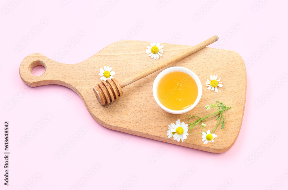 Wooden board with bowl of honey and chamomile flowers on pink background