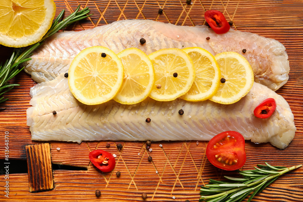 Raw codfish fillet with lemon on wooden background