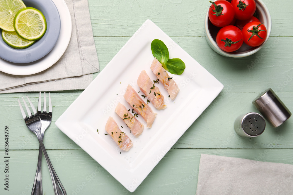 Plate with pieces of raw codfish fillet, lime and tomatoes on green wooden background