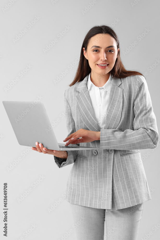 Young businesswoman in stylish suit using laptop on light background