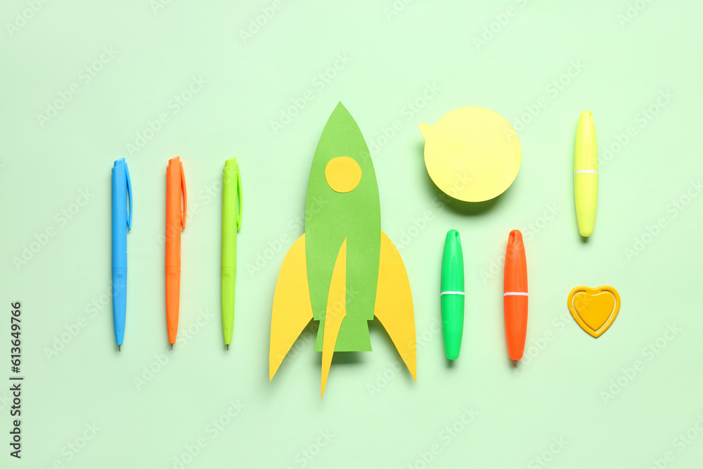 Paper rocket with different stationery and speech bubble on green background