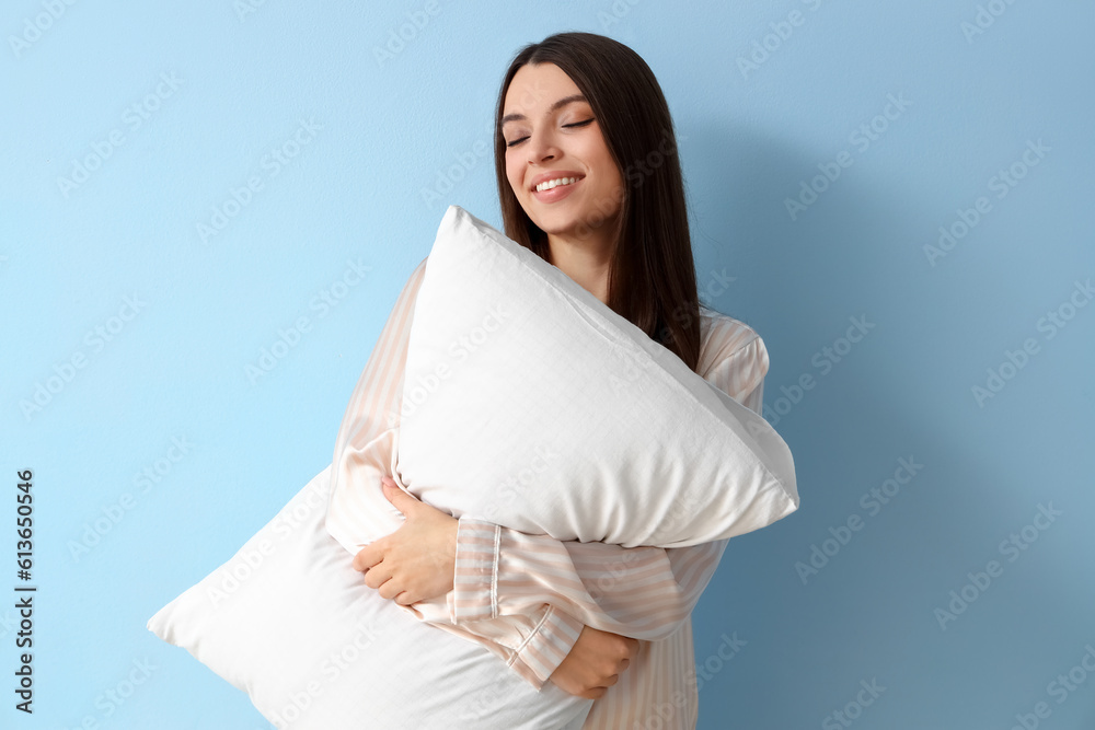 Young woman in pajamas with soft pillow on blue background