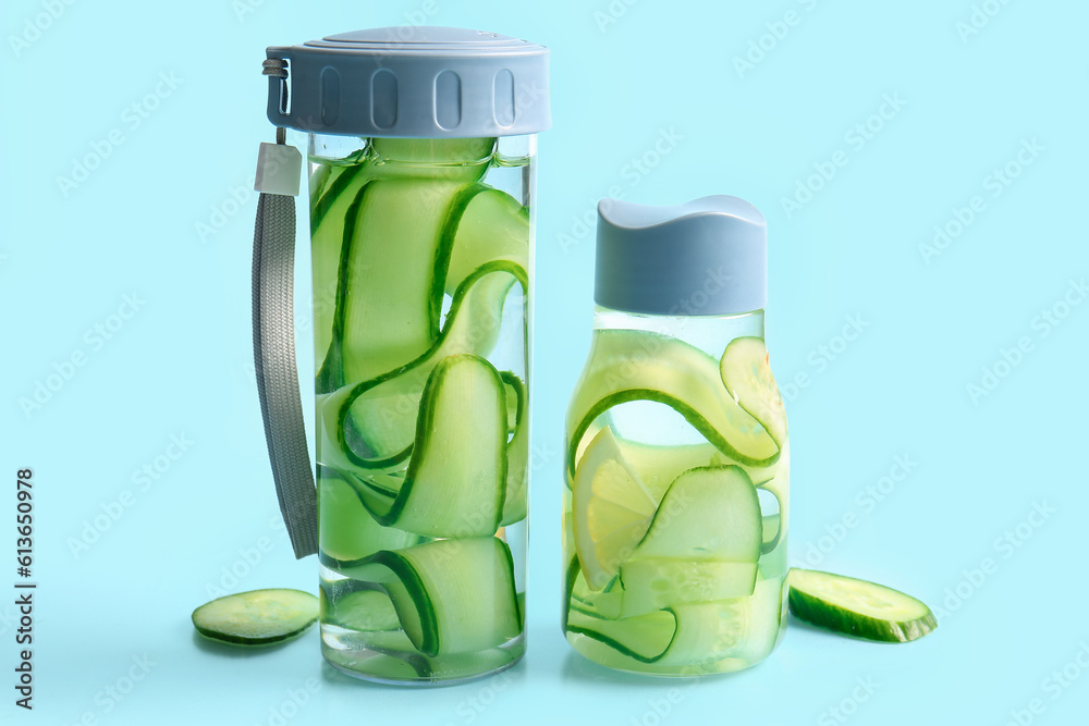 Sports bottles of infused water with cucumber slices on blue background