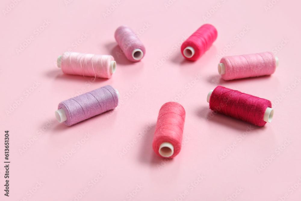 Frame made of different thread spools on pink background