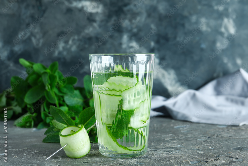 Glass of infused water with cucumber slices on grey table