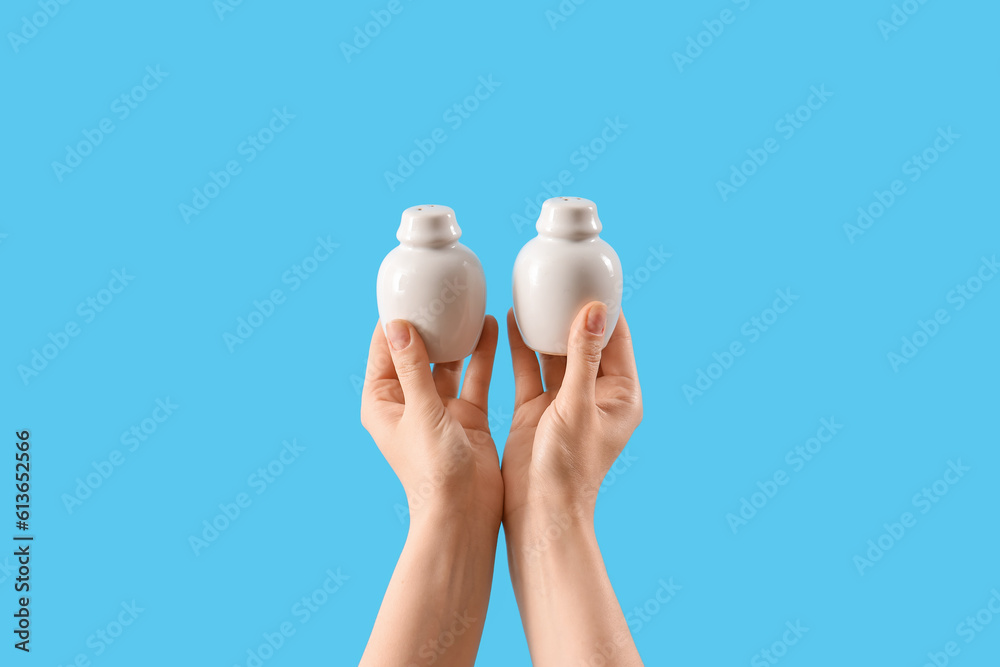 Female hands holding pepper and salt shakers on blue background