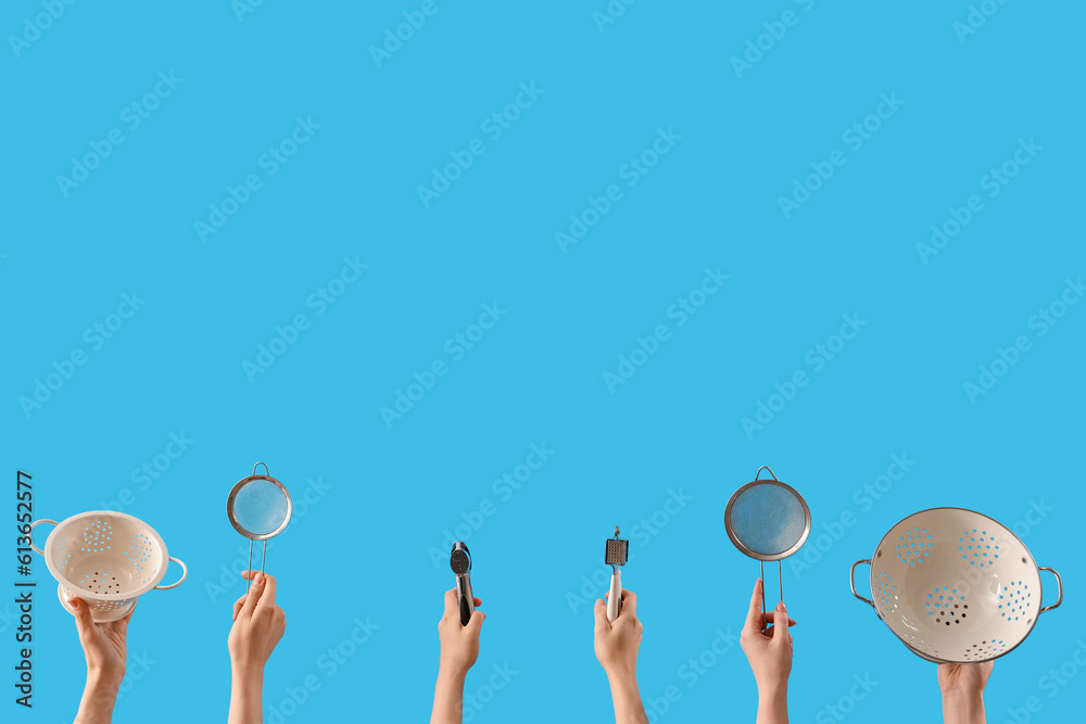 Female hands holding colanders, sieves and kitchen utensils on blue background